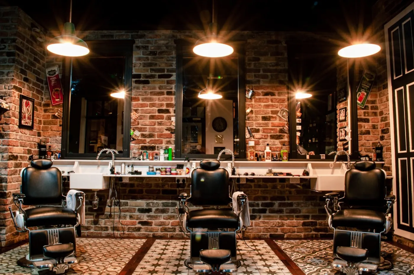 Salão da barbearia, com cadeiras de barbeiro e parede de tijolo.